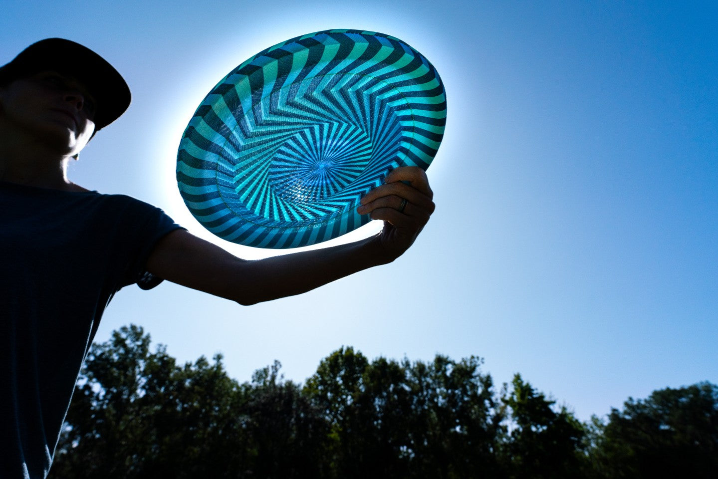 Latający dysk Waboba Bigwing trzymany przez osobę przed rzutem na tle błękitnego nieba