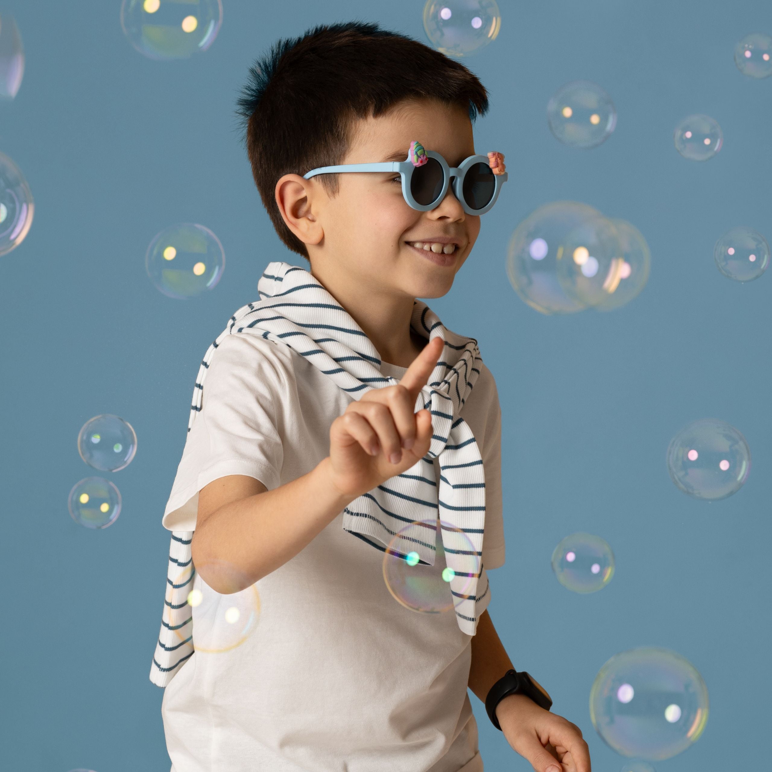Chłopiec w niebieskich okularach przeciwsłonecznych dla dzieci bawiący się z bańkami mydlanymi