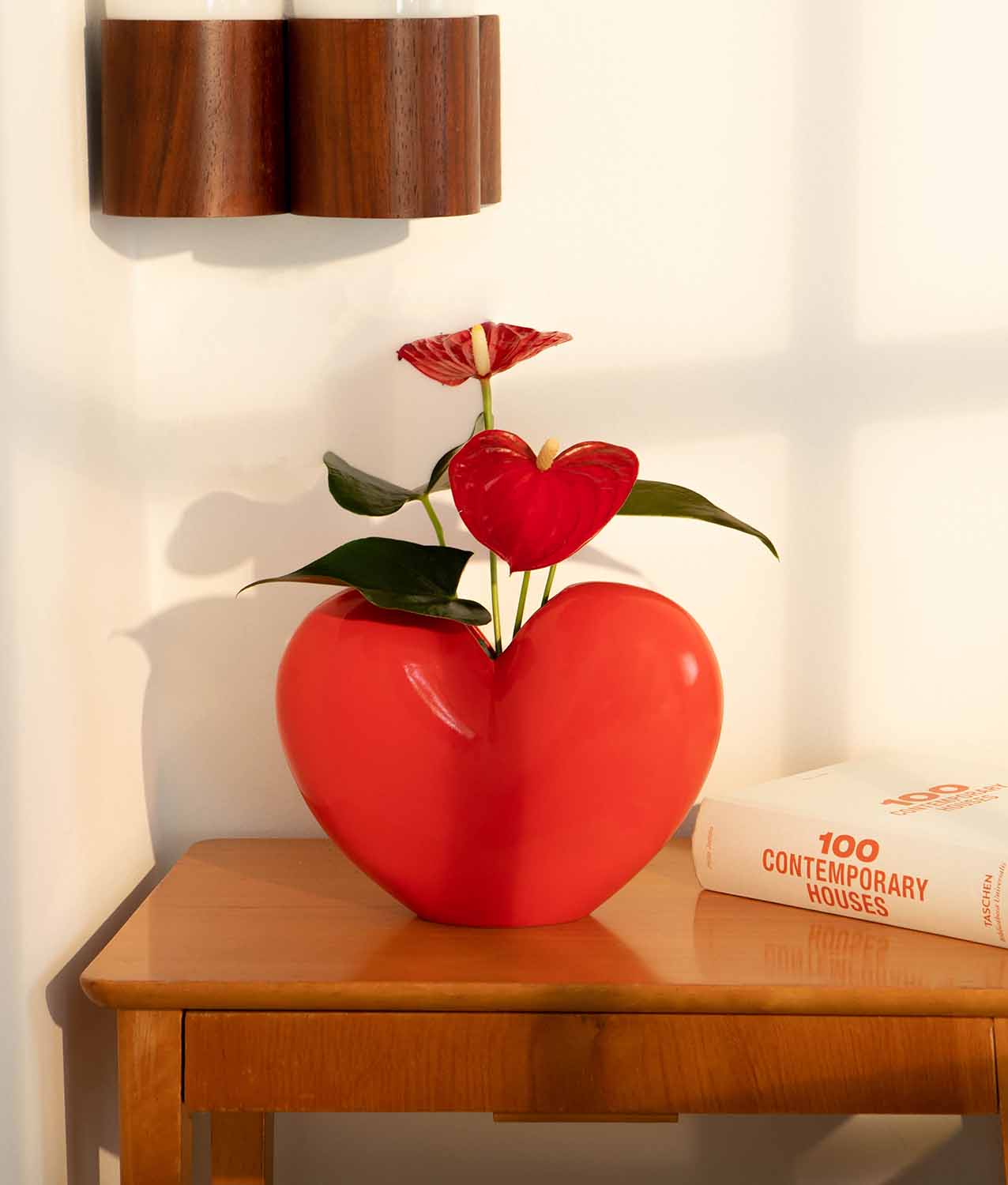 Czerwony wazon dekoracyjny czerwone serce na drewnianym stoliku z kwiatem i książką obok