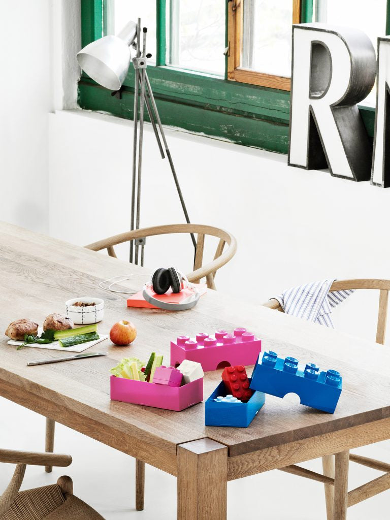 Lunchbox klocek LEGO różowy i niebieski na drewnianym stole z przekąskami w nowoczesnym wnętrzu