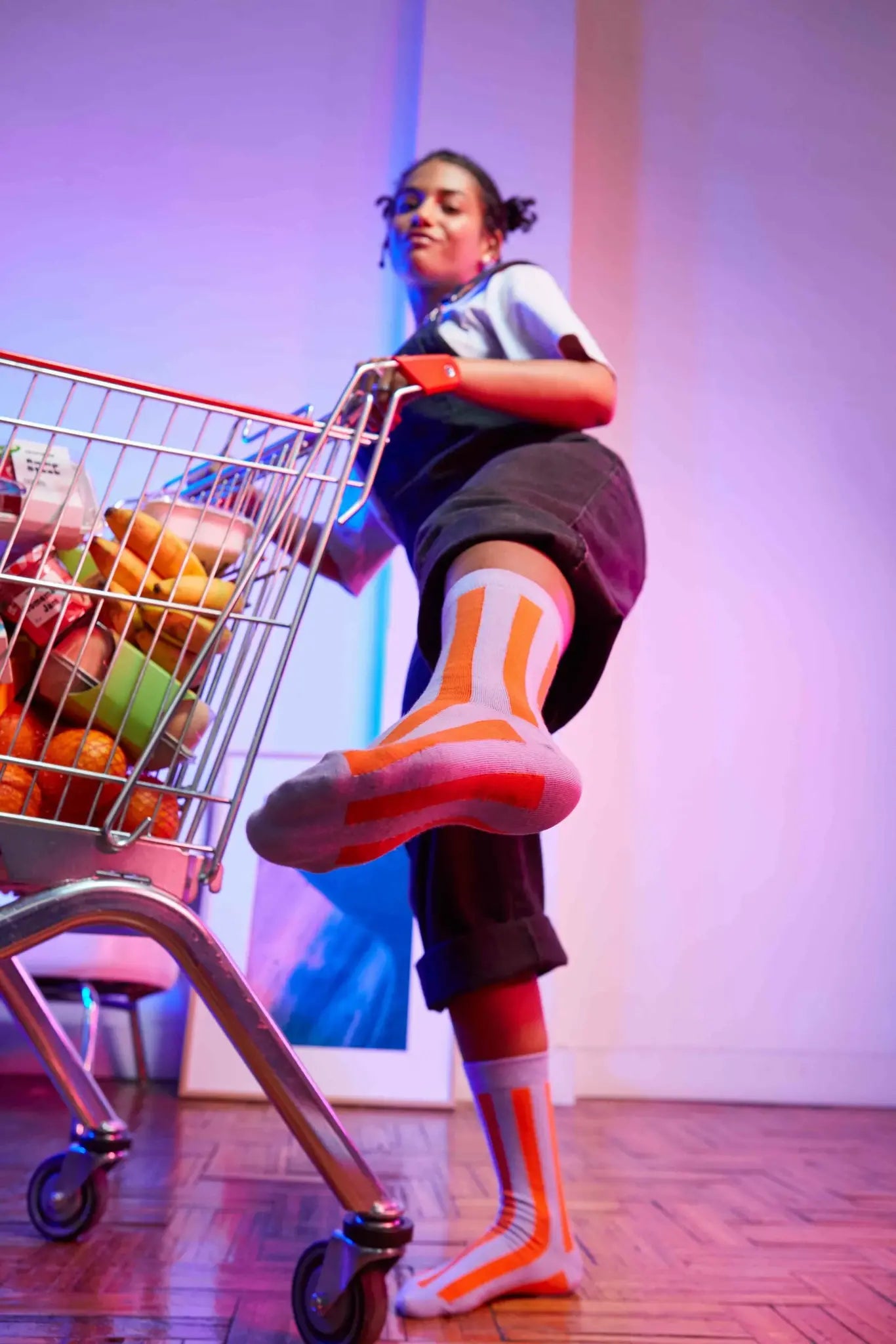 Młoda kobieta w modnych skarpetkach łosoś Eat My Socks z pomarańczowymi paskami przy wózku sklepowym