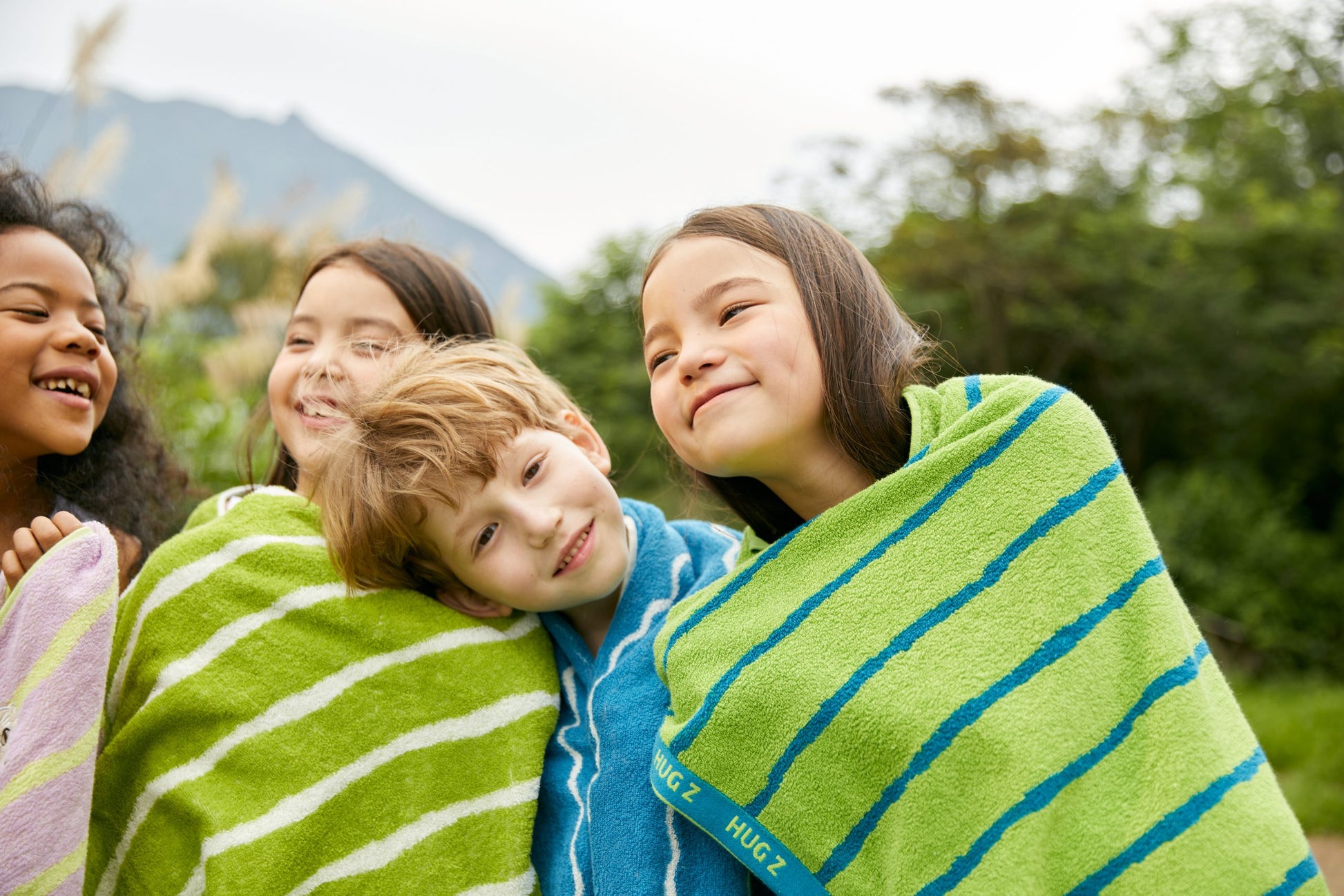 Grupa dzieci owiniętych w kolorowe ręczniki kąpielowe dla dzieci na zewnątrz na tle zieleni