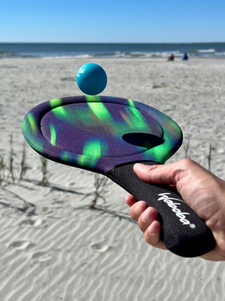 Kolorowa paletka do gry na plaży trzymana w dłoni z niebieską piłką i napisem Waboba paletki plażowe Waboba