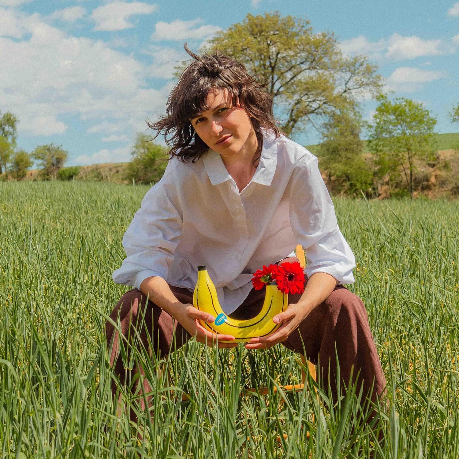 Kobieta w białej koszuli trzyma wazon dekoracyjny żółty banan z czerwonymi kwiatami na łące