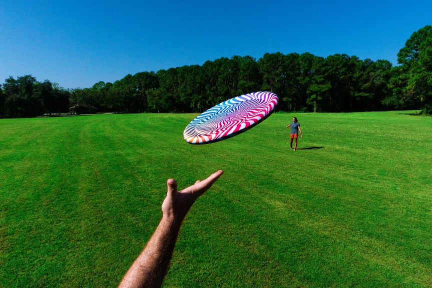 Latający dysk Waboba Bigwing w kolorowy wzór rzucany na zielonym polu przez osobę