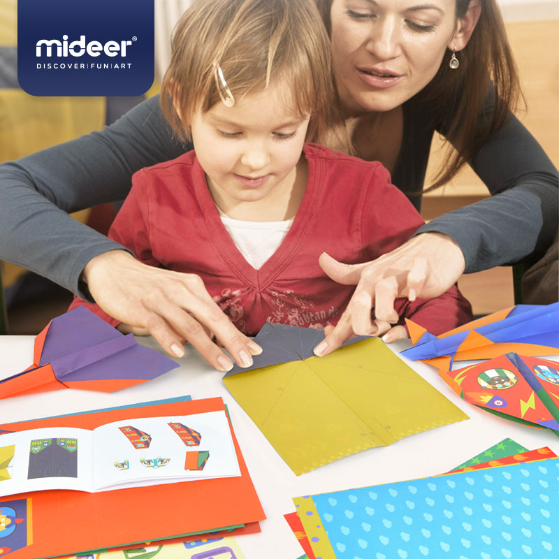 Kobieta i dziecko składają origami samoloty papierowe na stole z kolorowymi kartkami i instrukcjami