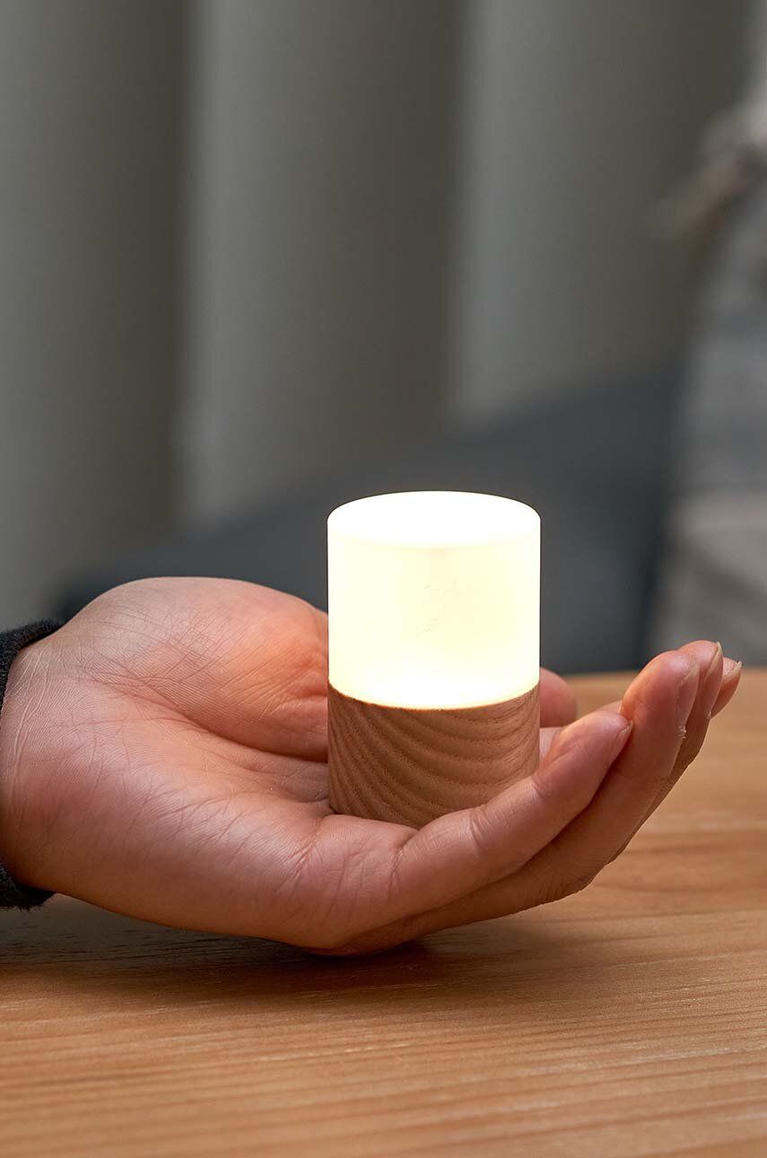 Lampka nocna z drewna jesionowego trzymana w dłoni na drewnianym stole, emitująca miękkie światło