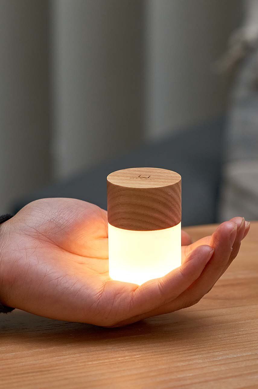 Lampka nocna z drewna jesionowego trzymana w dłoni emitująca ciepłe światło na stole