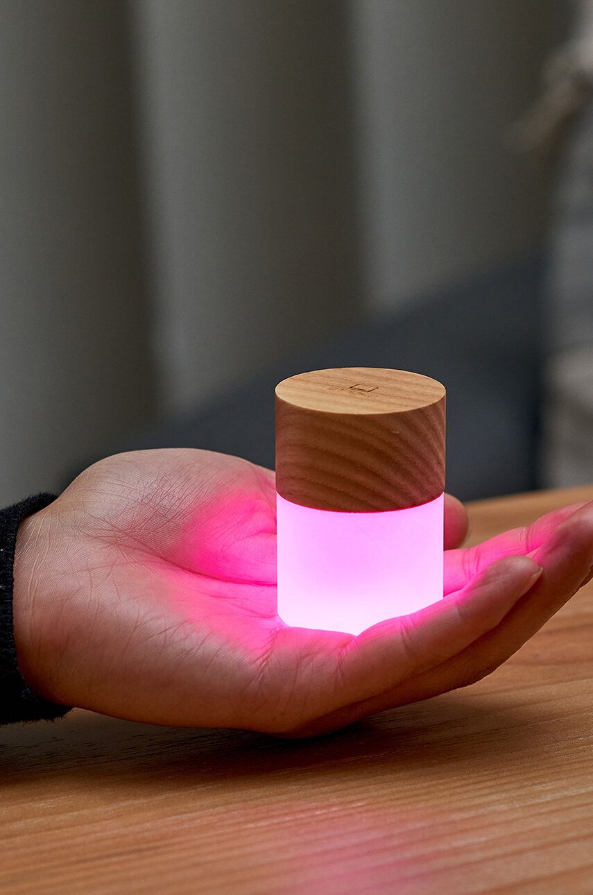 Lampka nocna z drewna jesionowego o kompaktowym kształcie emitująca różowe światło na dłoni