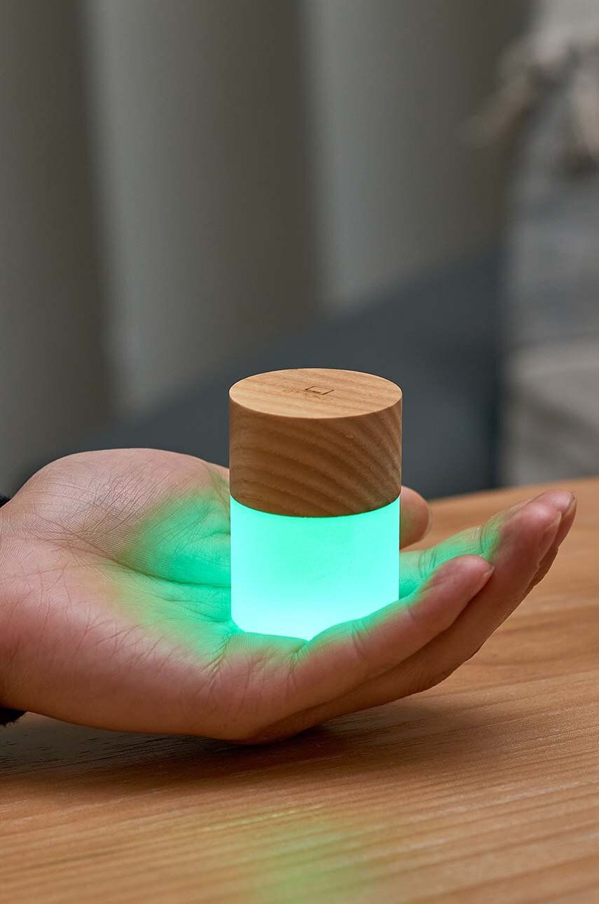 Lampka nocna z drewna jesionowego WABOBA AB trzymana na dłoni z zielonym światłem