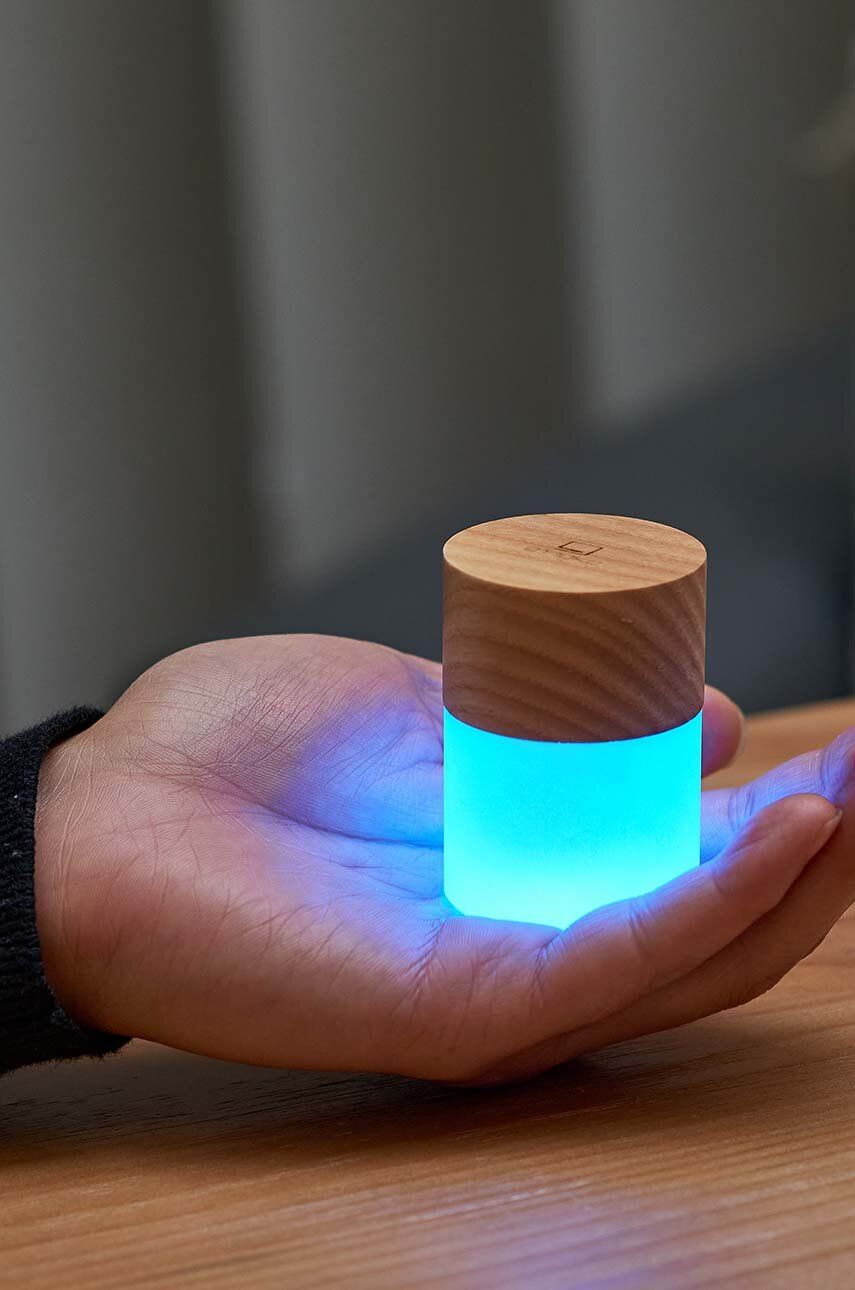 Lampka nocna z drewna jesionowego o kompaktowym rozmiarze emitująca delikatne niebieskie światło w dłoni