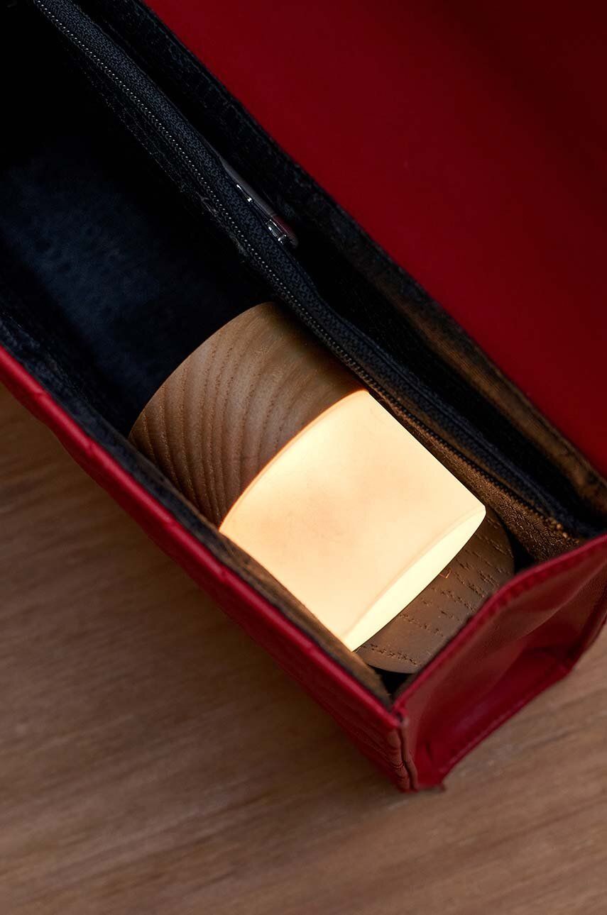 Lampka nocna z drewna jesionowego o minimalistycznym designie umieszczona w czerwonej saszetce