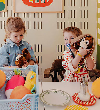 Dzieci bawią się maskotką małpa kokos w domowym pokoju z kolorowymi zabawkami na stole