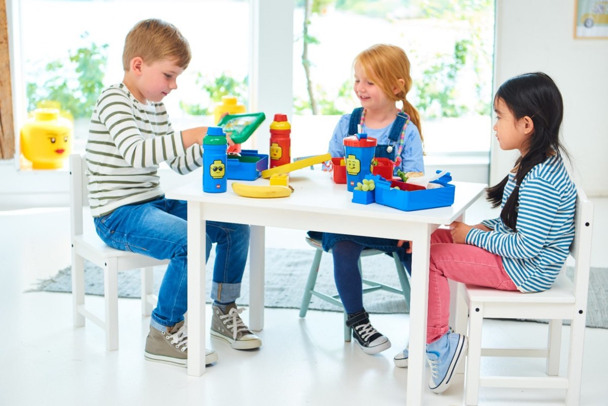 Bidon LEGO dla dziewczynki na stole obok dzieci bawiących się klockami w jasnym pokoju