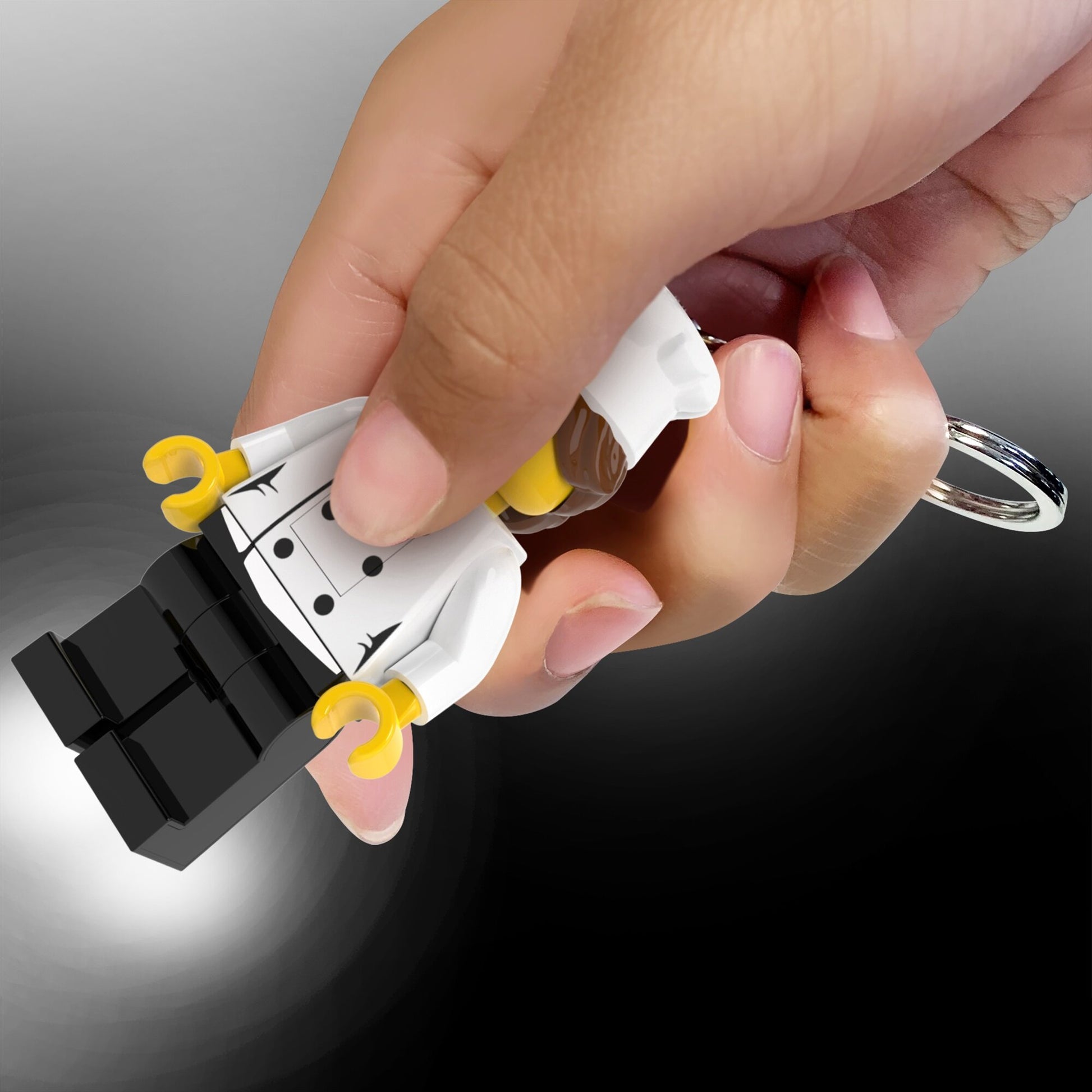 brelok z latarką LEGO kucharka trzymany w dłoni z włączoną latarką na czarnym tle