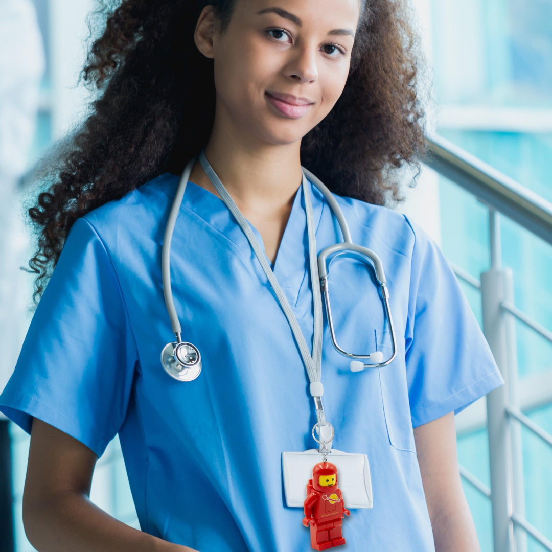 Brelok LEGO czerwony astronauta przypięty do identyfikatora na szyi kobiety w niebieskim ubraniu medycznym