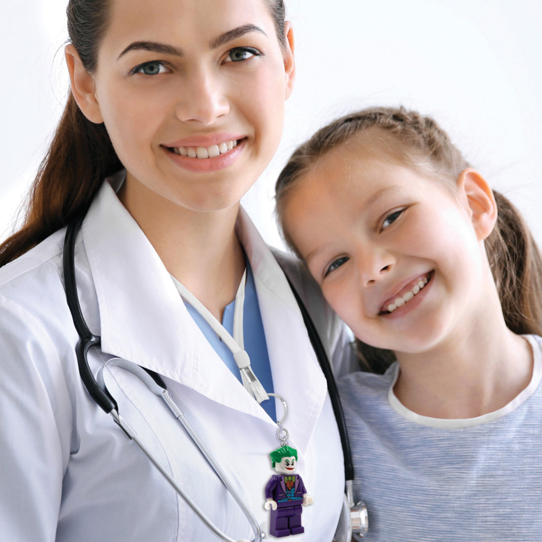 brelok LEGO Joker z latarką przypięty do białego fartucha lekarza z uśmiechniętą dziewczynką