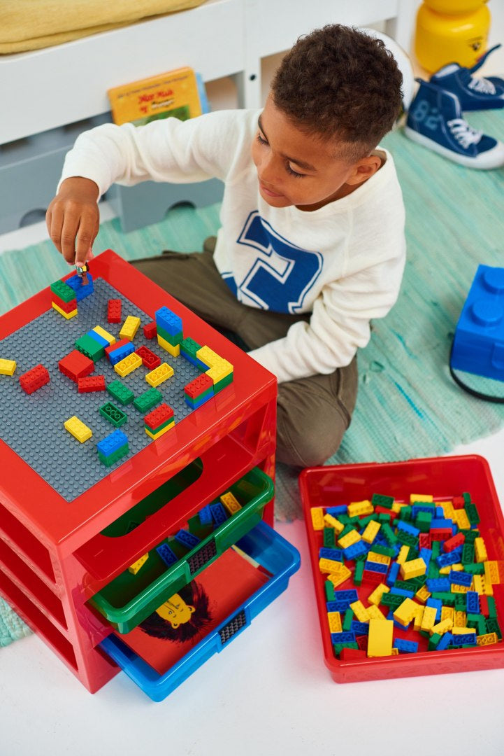 Dziecko bawiące się kolorowymi klockami na czerwonym regale LEGO z szufladami w pokoju dziecięcym