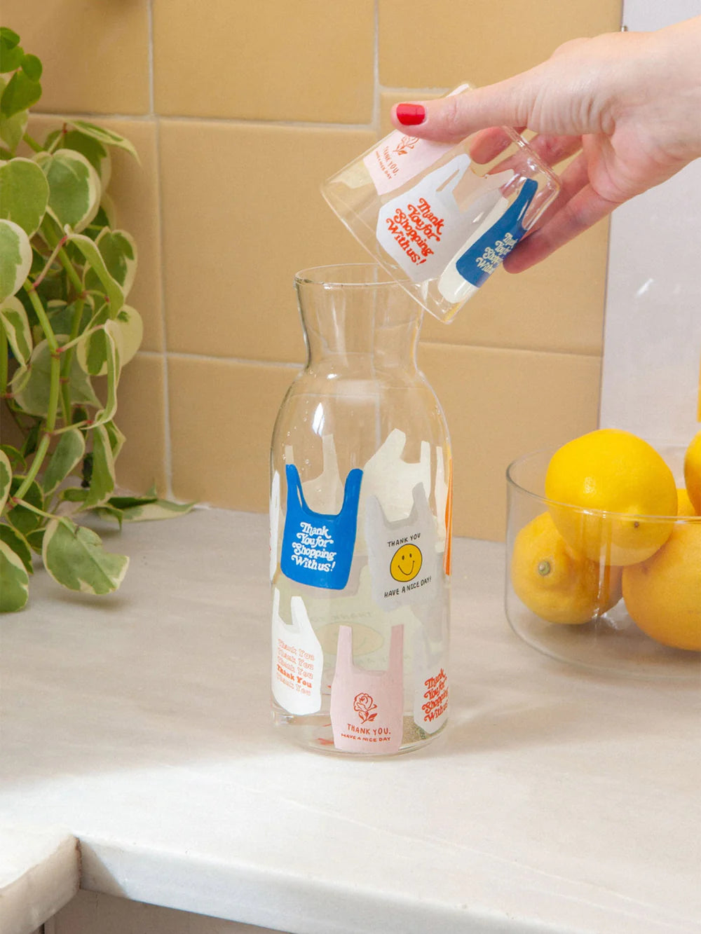 Karafka i szklanka z nadrukiem z kolorowymi wzorami na białym stole obok cytryn