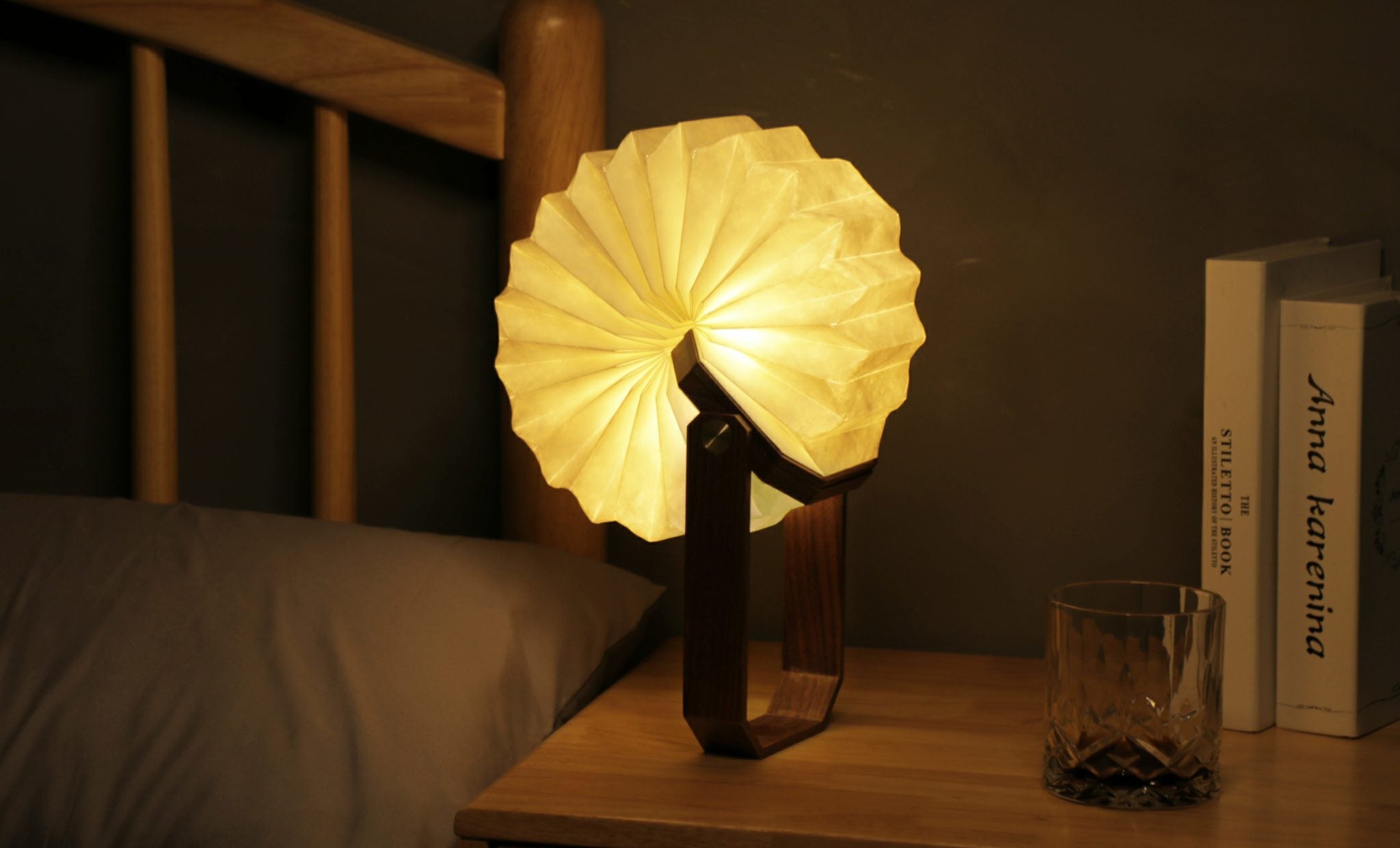 Inteligentna lampa origami orzech na stoliku nocnym obok szklanki i książek przy łóżku