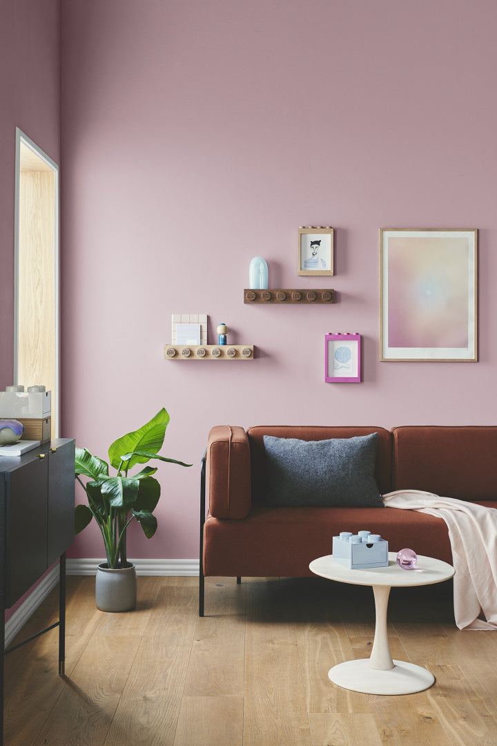 drewniana półka LEGO zamontowana na różowej ścianie nad brązową sofą w nowoczesnym salonie