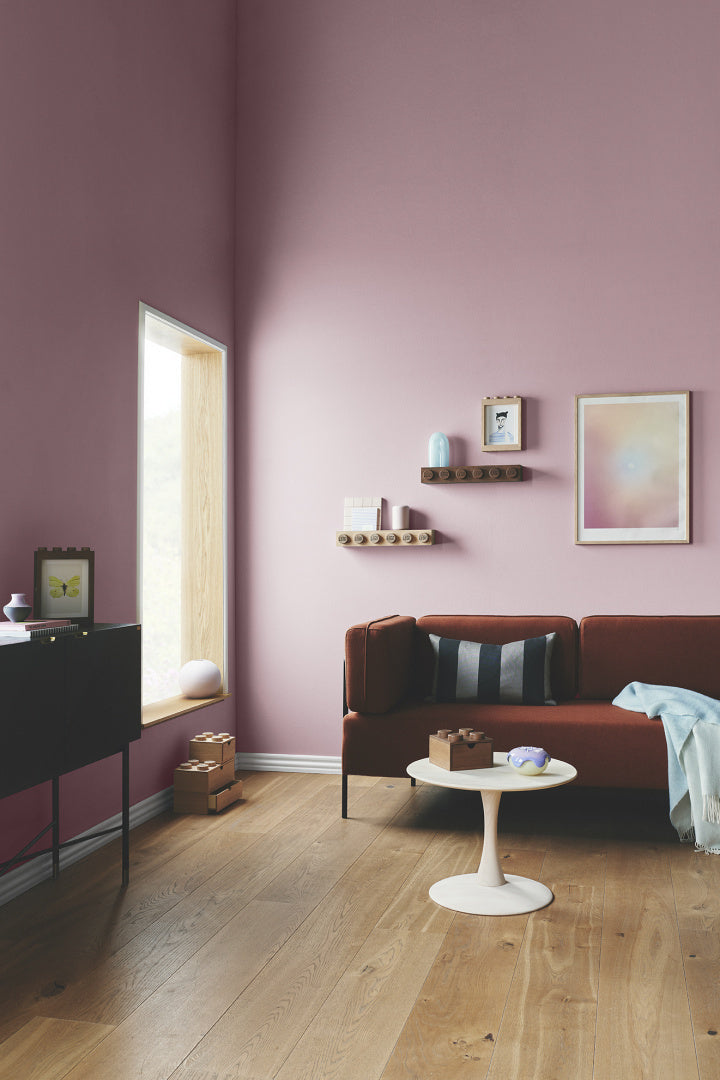 Nowoczesny salon z bordową sofą i drewnianą półką LEGO na różowej ścianie