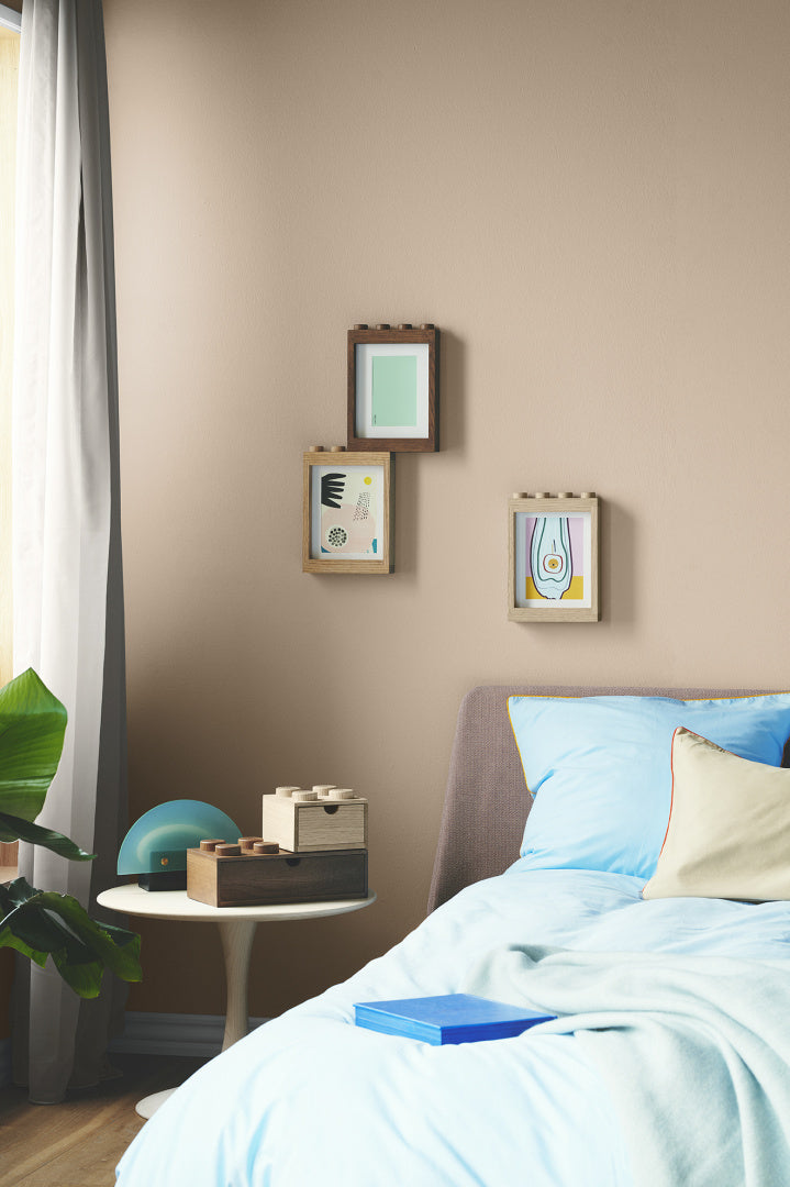 Trzy drewniane ramki LEGO na zdjęcia zawieszone na ścianie w sypialni obok łóżka z niebieską pościelą