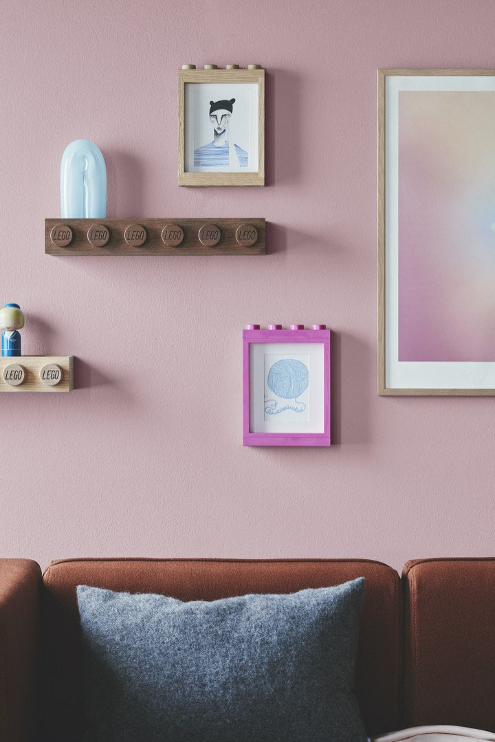 Drewniana ramka LEGO na zdjęcia w naturalnym i różowym kolorze zamontowana na ścianie nad kanapą