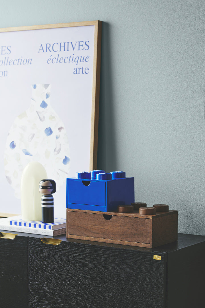 Drewniana szufladka LEGO na biurko w brązowym i niebieskim kolorze na czarnej komodzie