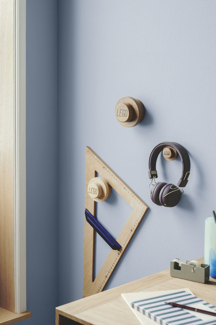 Naturalne drewniane wieszaki LEGO zamontowane na niebieskiej ścianie z słuchawkami i linijką
