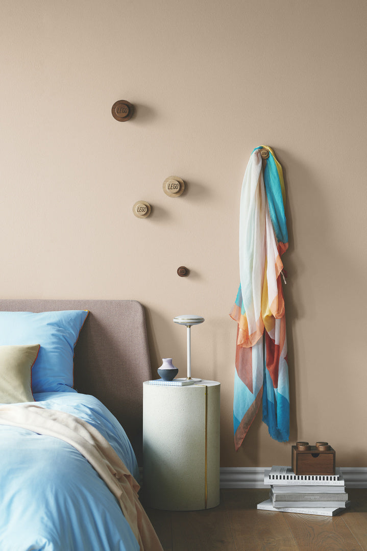 Drewniane wieszaki LEGO na ścianie obok łóżka z niebieską pościelą w nowoczesnej sypialni