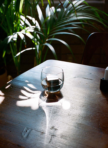 Szklanka z wodą i kostką do napojów design na drewnianym stole przy zielonych roślinach