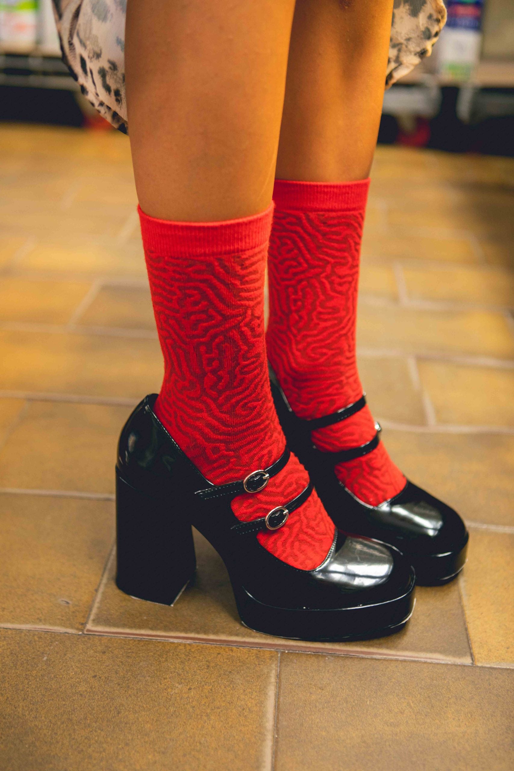 Czerwone skarpetki w kształcie kiełbasy chorizo na stopach w czarnych lakierowanych butach na obcasie