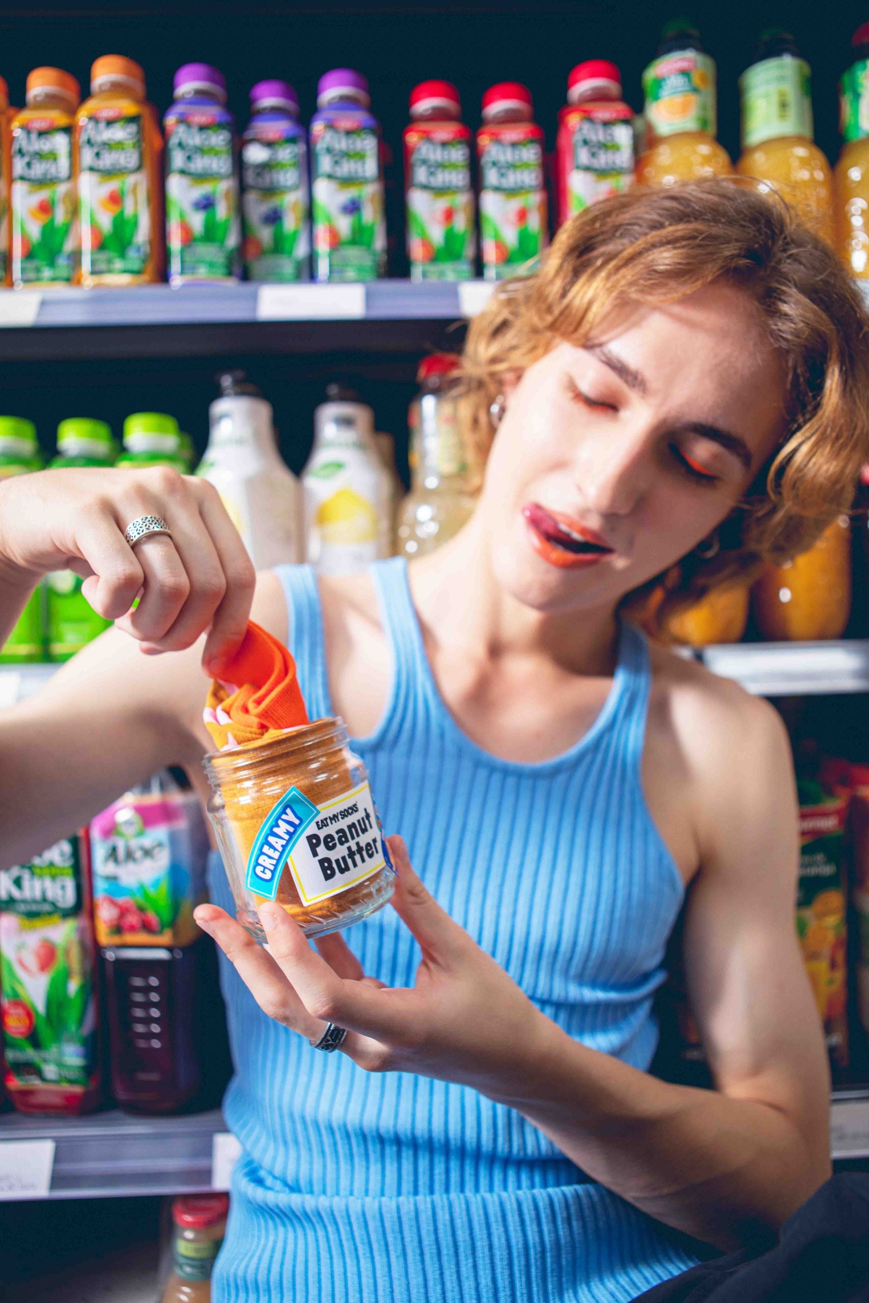 Kobieta w niebieskim topie wyjmuje skarpetki peanut butter z słoika masła orzechowego na tle sklepowych półek