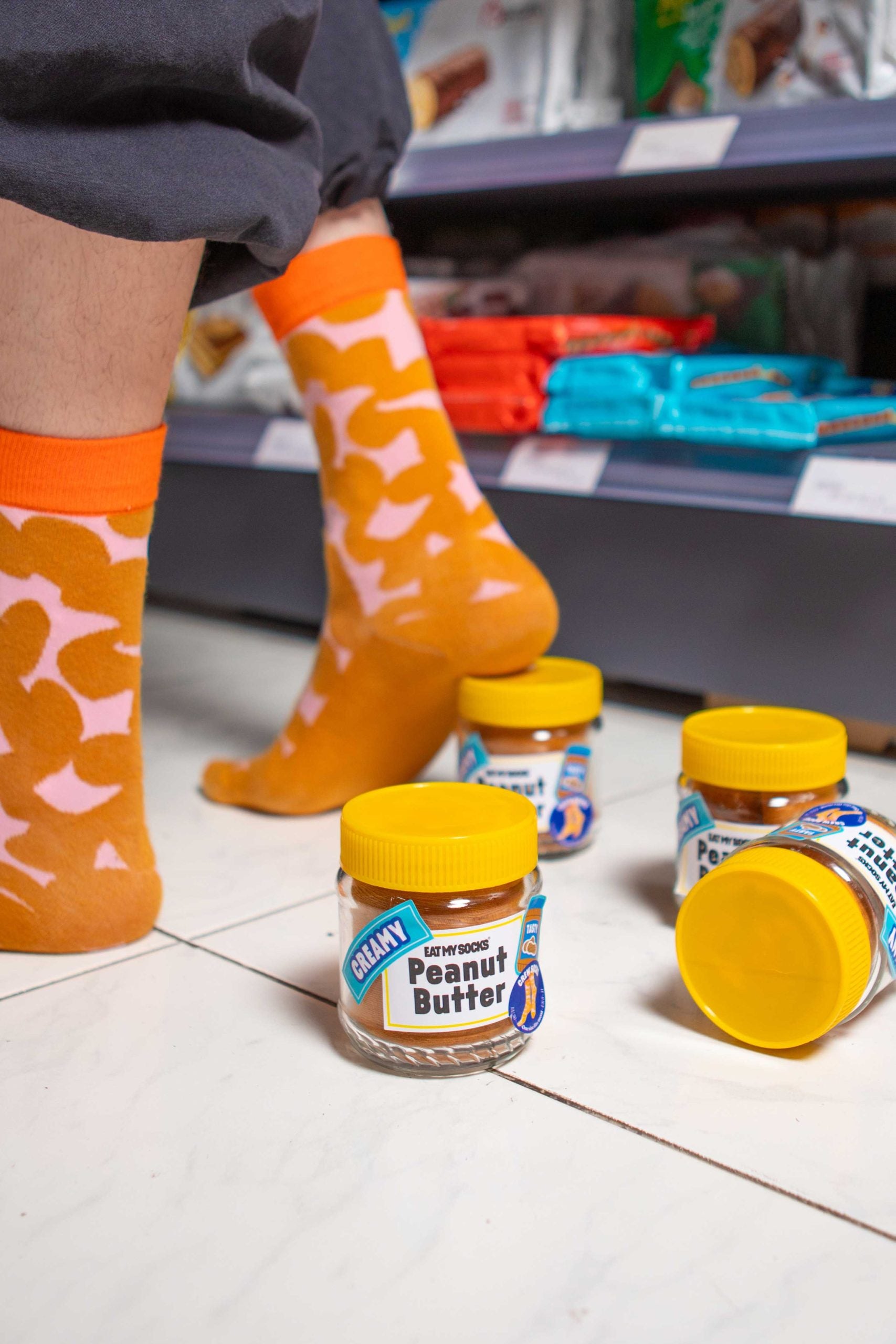 Pomarańczowe skarpetki peanut butter z wzorem orzeszków na tle słoików masła orzechowego EMS