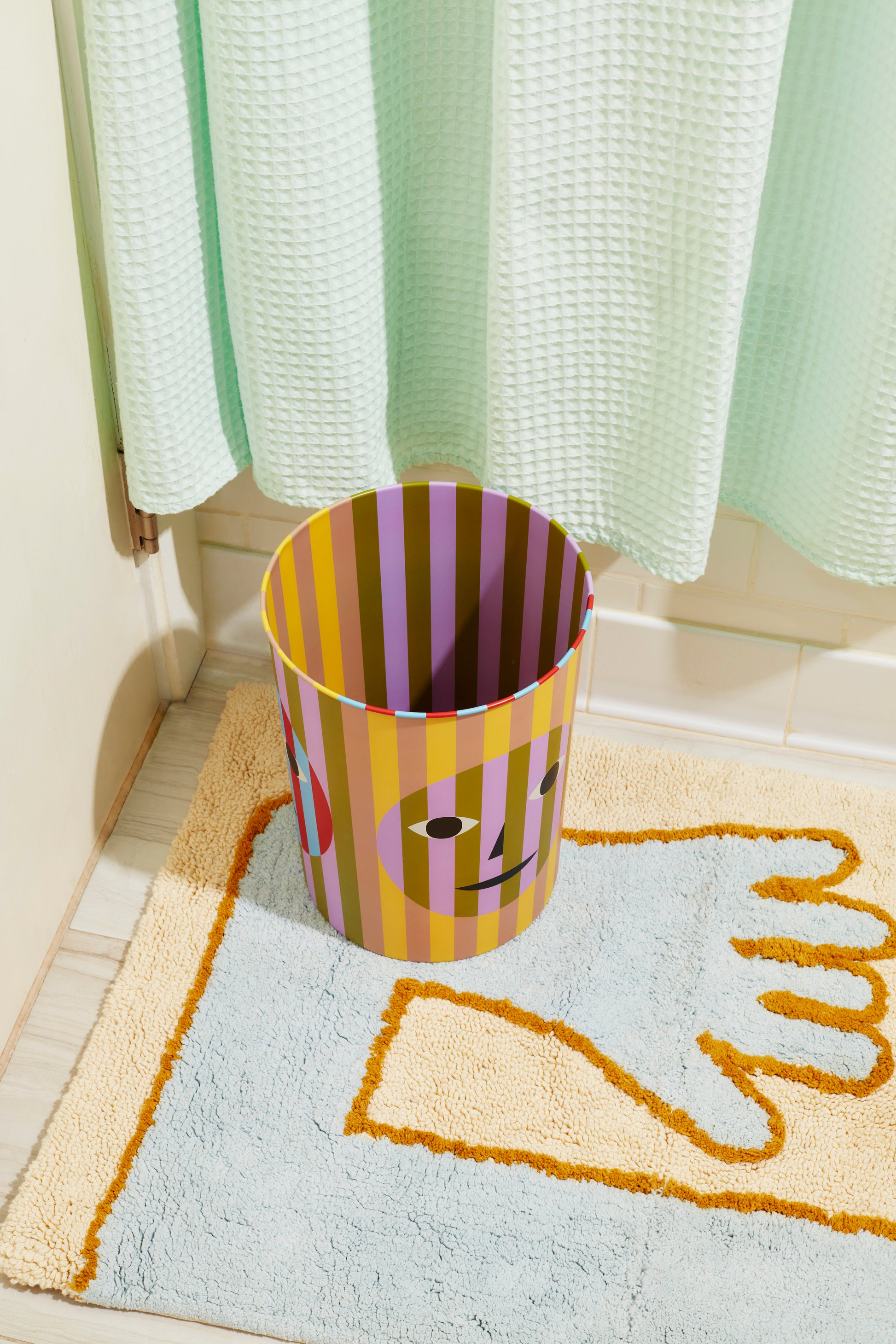 Kolorowy kosz na śmieci design z twarzą i paskami postawiony na dywanie w łazience
