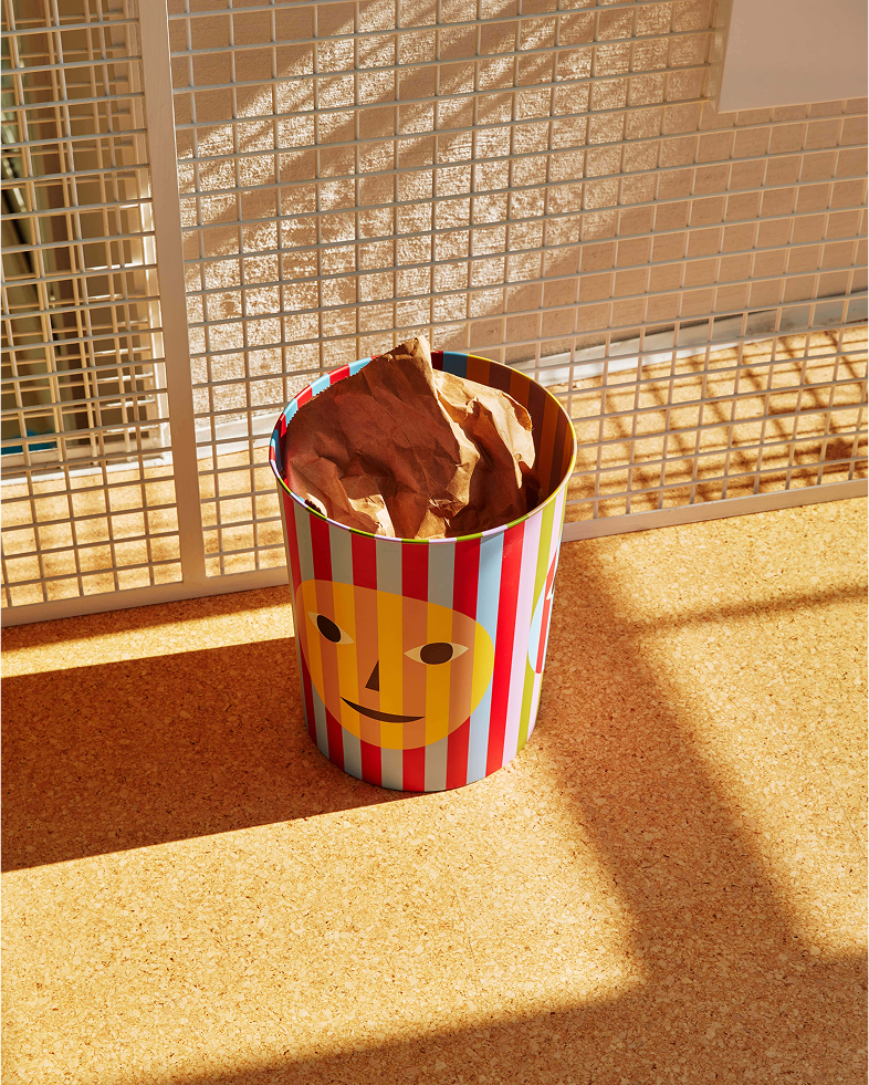 Kolorowy kosz na śmieci design Areaware z paskami i uśmiechniętą twarzą na jasnej podłodze