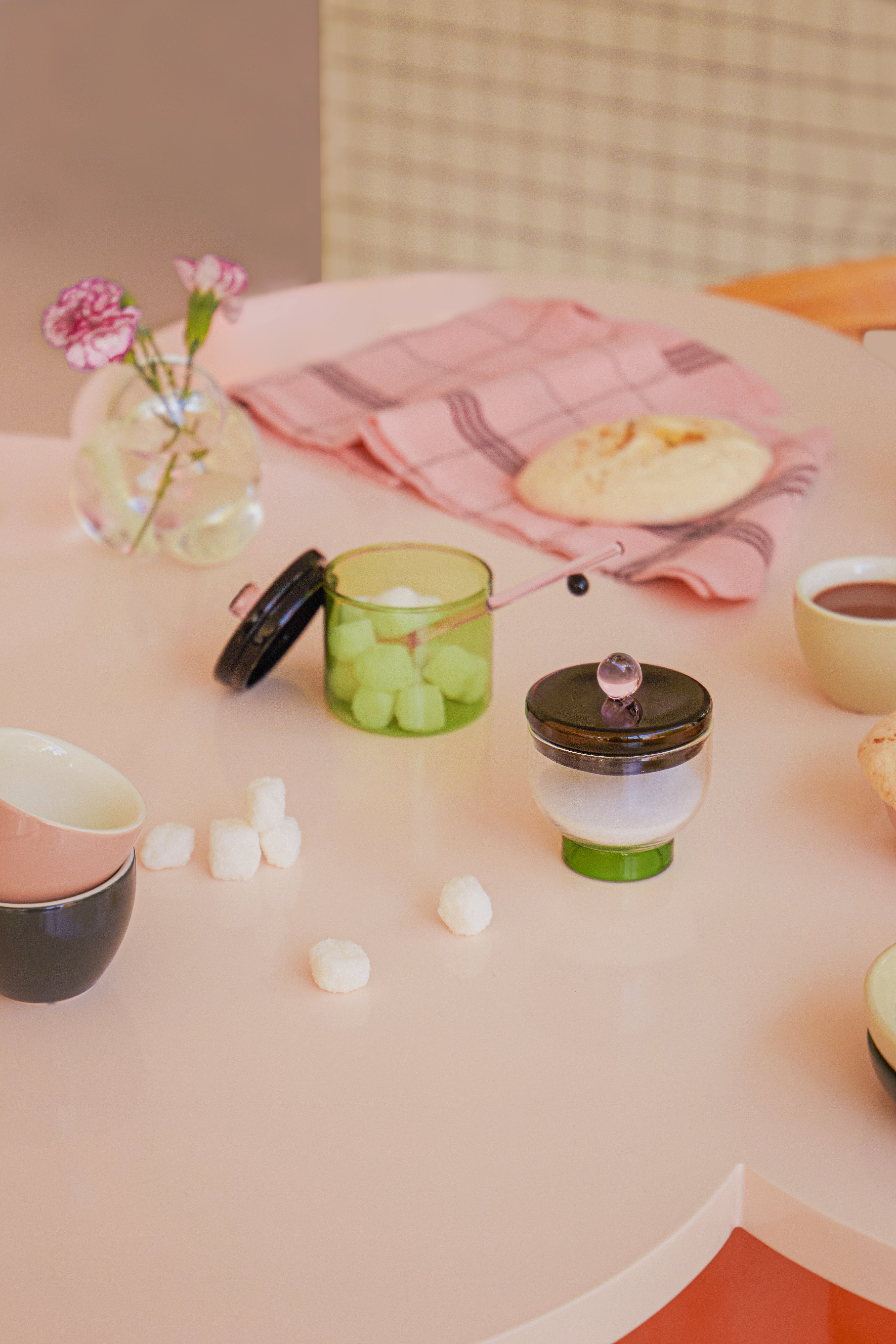 Miseczka na sól szklana z pokrywką i łyżeczką na stole z różowymi i zielonymi dodatkami