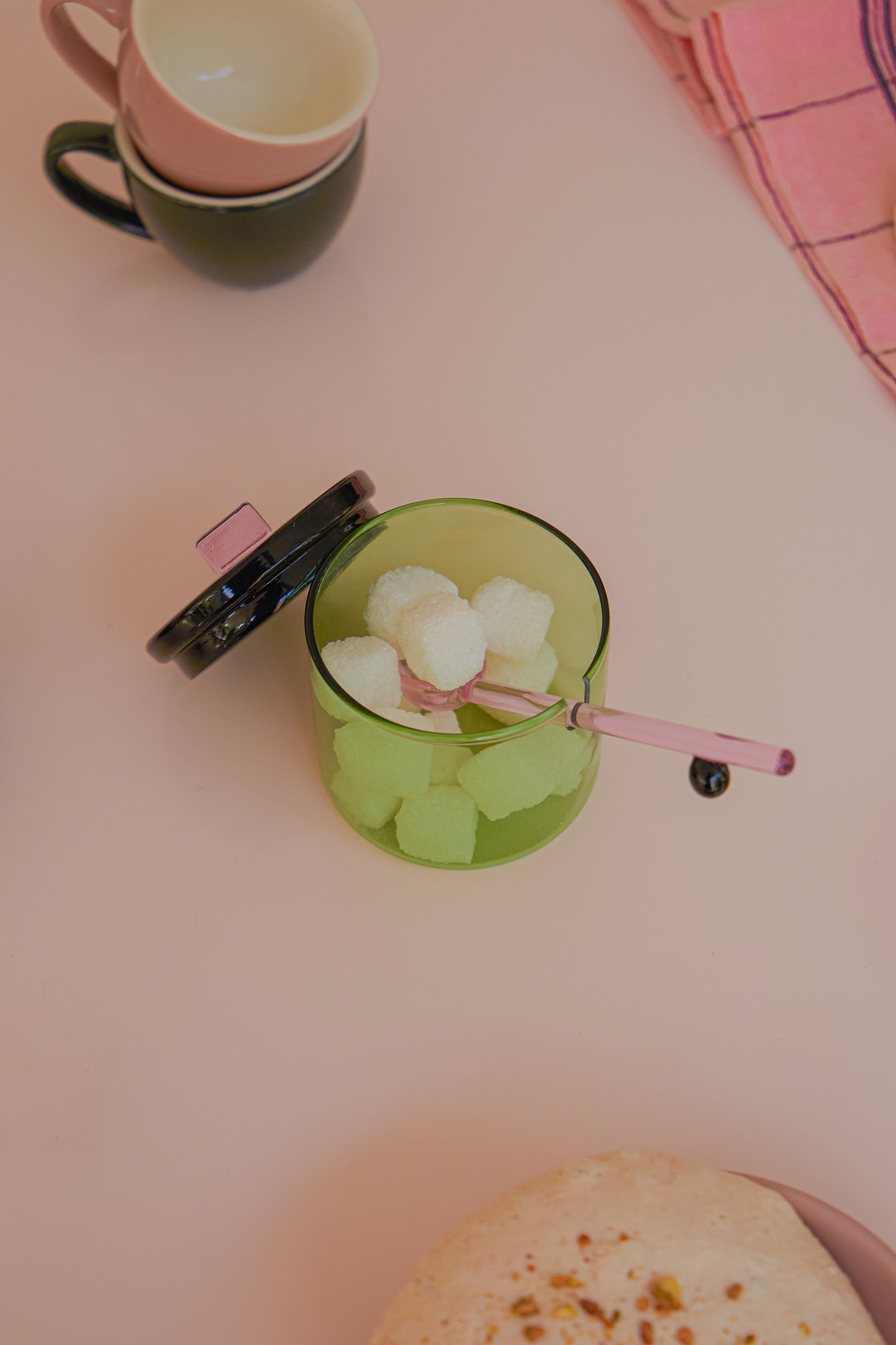 Zielona miseczka na cukier Areaware z pokrywką i łyżeczką na cukierki obok filiżanek i serwetki