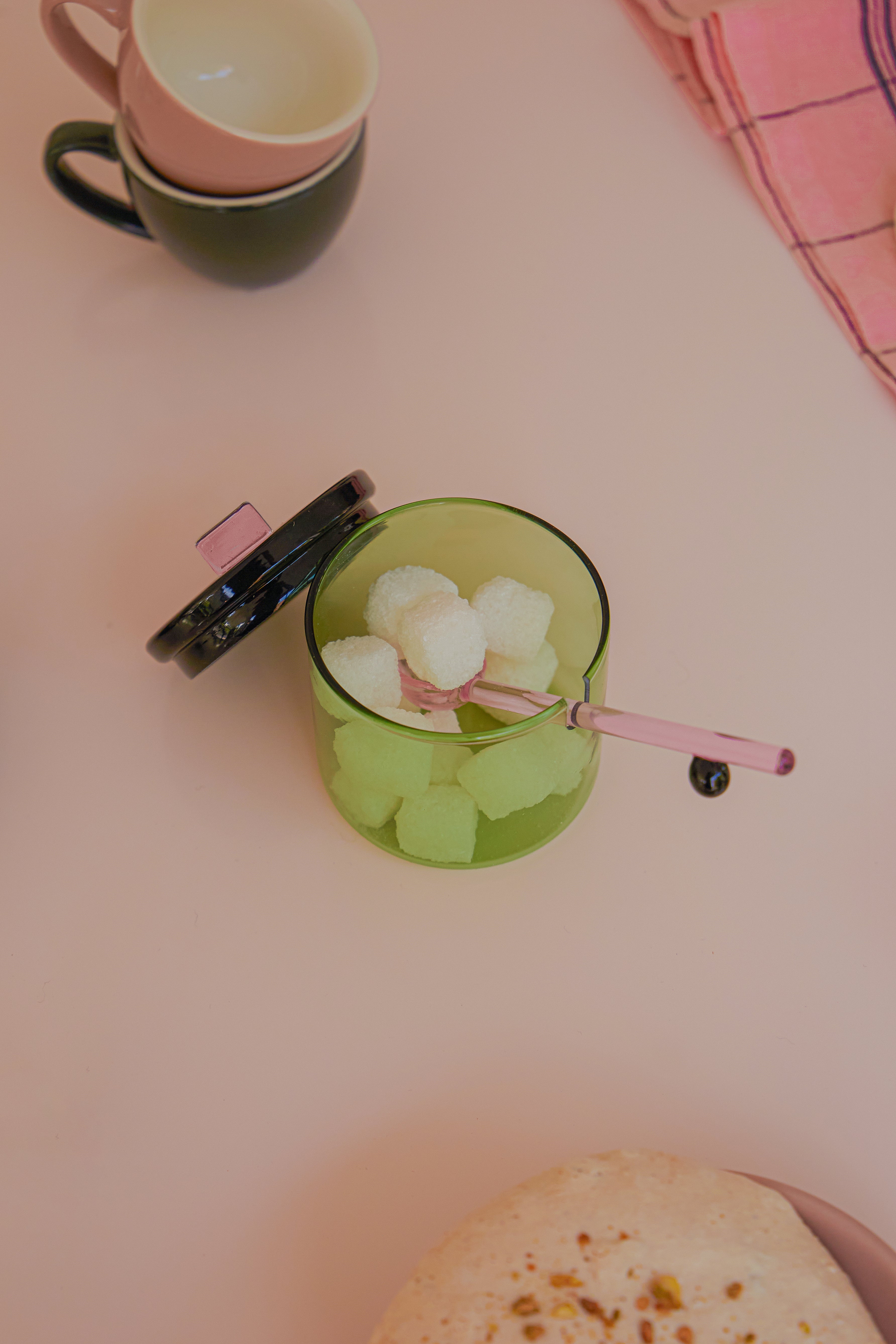 Zielona miseczka na cukier Areaware z pokrywką i łyżeczką na cukierki obok filiżanek i serwetki