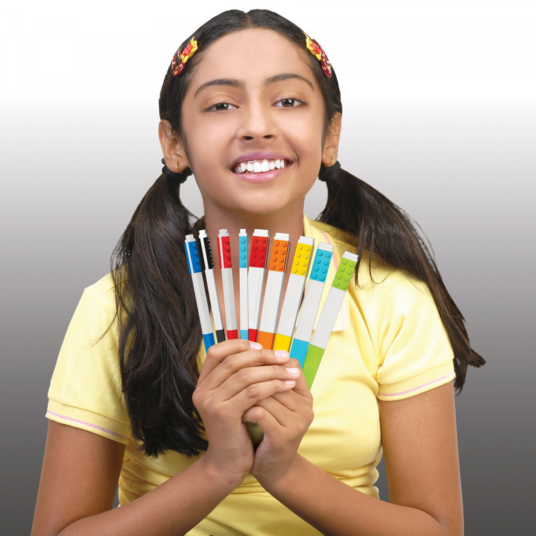 Dziewczynka trzyma flamastry LEGO 12 kolorów w dłoniach uśmiechnięta na szarym tle