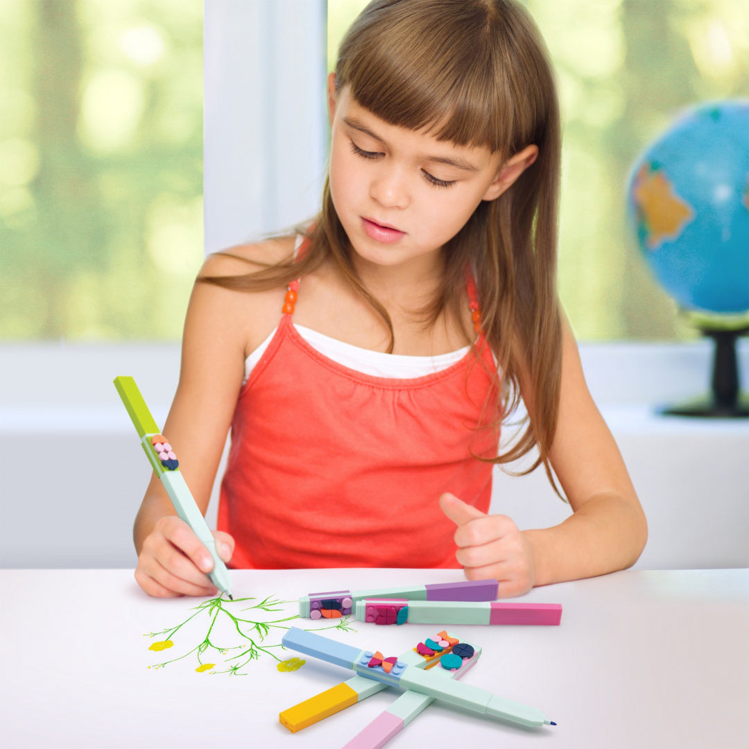 Dziewczynka rysująca z flamastrami LEGO DOTS w jasnym pokoju z globusem w tle