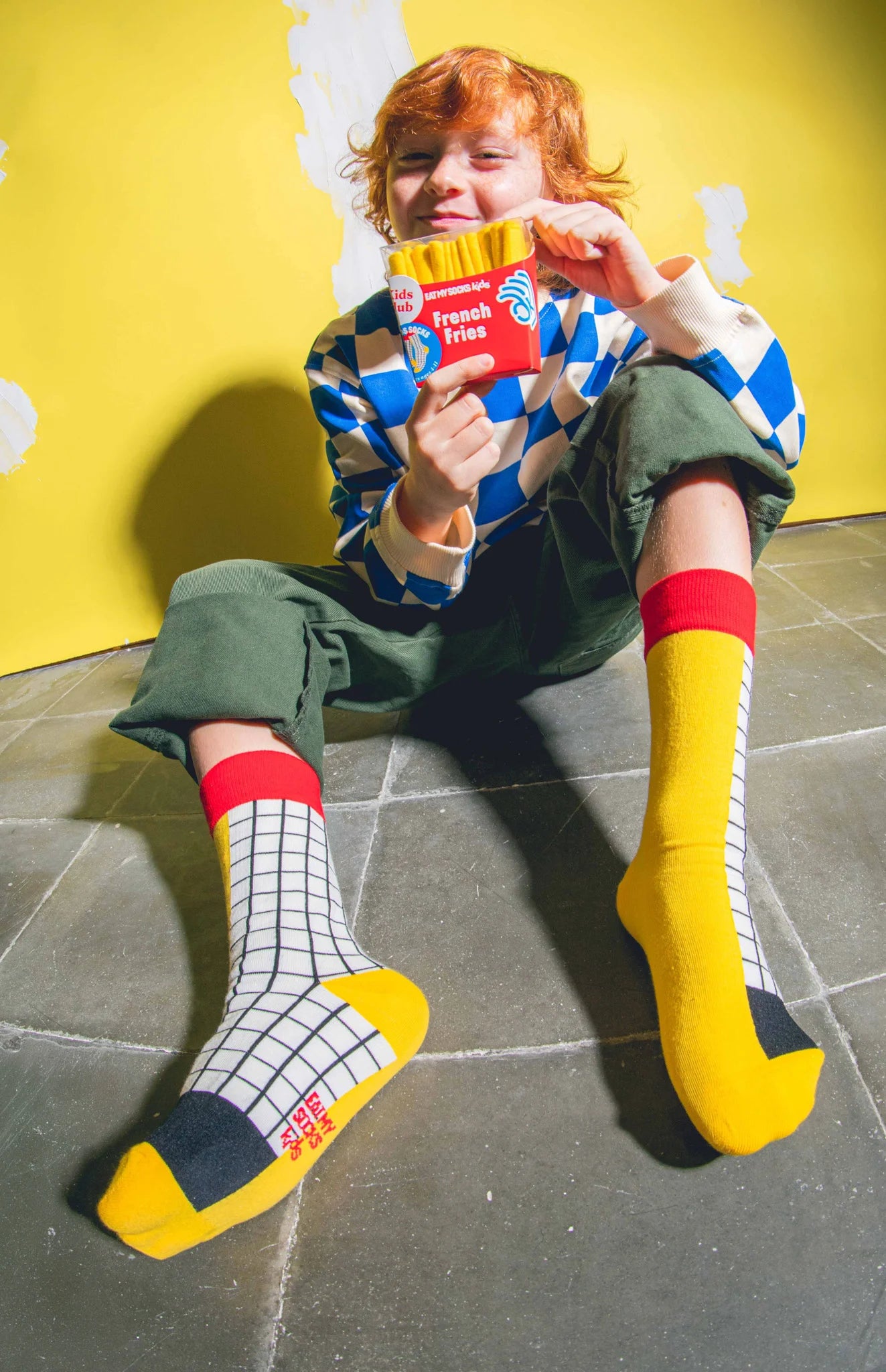 Kolorowe skarpetki frytki dla dzieci EMS noszone przez osobę siedzącą na podłodze z opakowaniem frytek