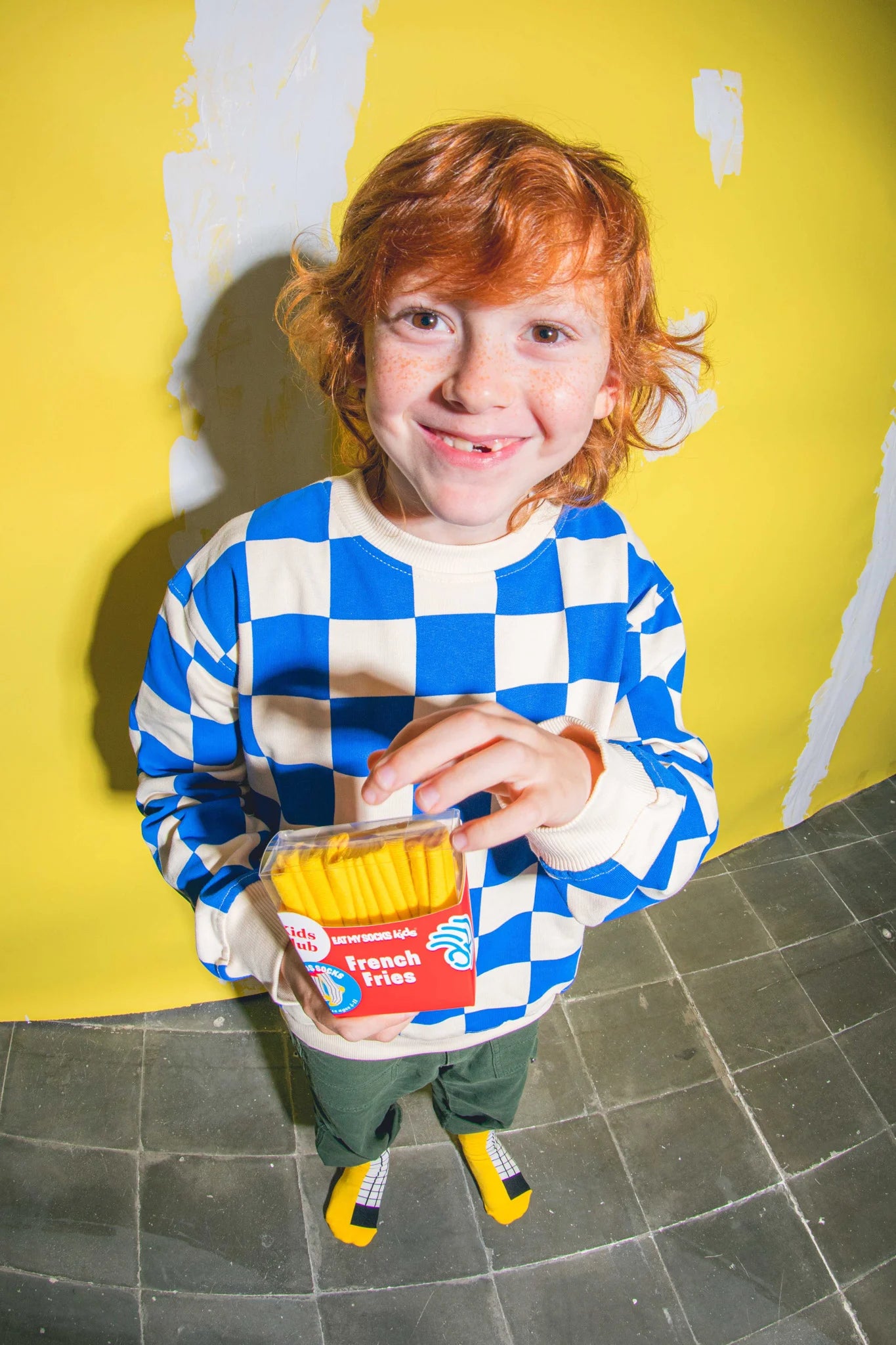 Dziecko w skarpetkach frytki dla dzieci EMS trzyma pudełko frytek stojąc na szarych płytkach