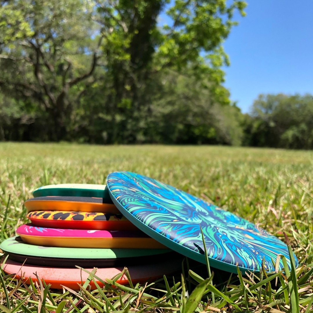 Kolorowe frisbee Waboba Wingman ułożone na trawie na tle zielonych drzew i niebieskiego nieba