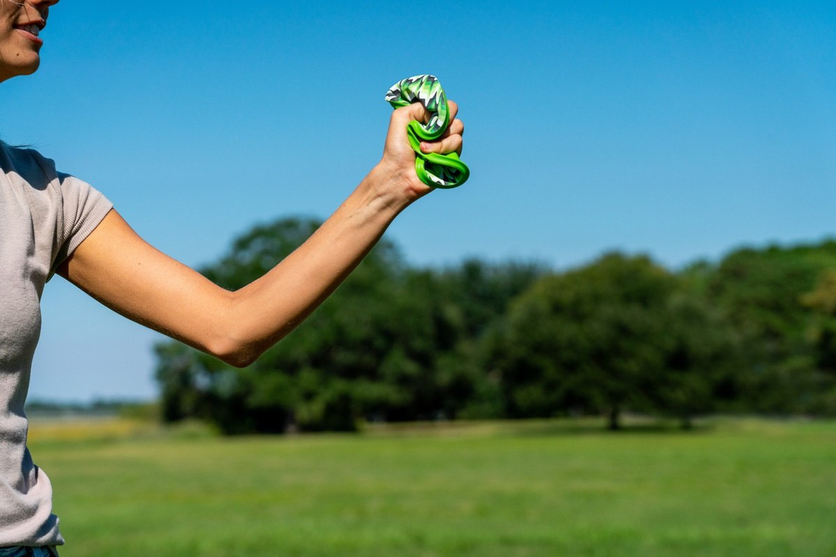 Osoba ściskająca zielony frisbee Waboba Wingman na tle zielonego pola i niebieskiego nieba