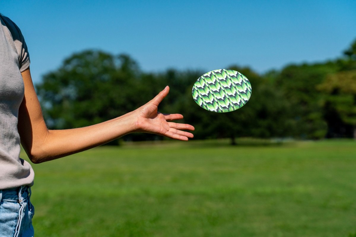 Osoba rzucająca frisbee Waboba Wingman na zielonym polu pod niebieskim niebem