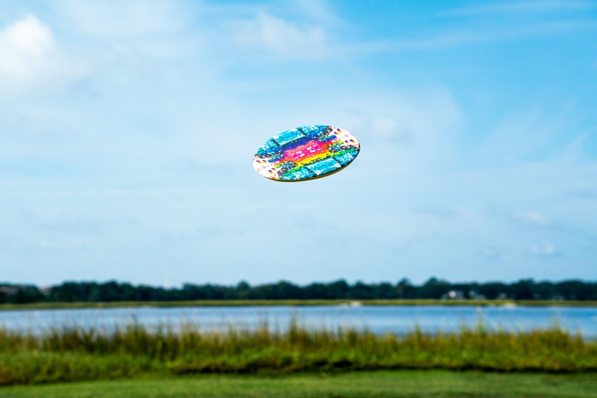 Kolorowy frisbee Waboba Wingman Pro unoszący się w powietrzu nad zieloną łąką i jeziorem