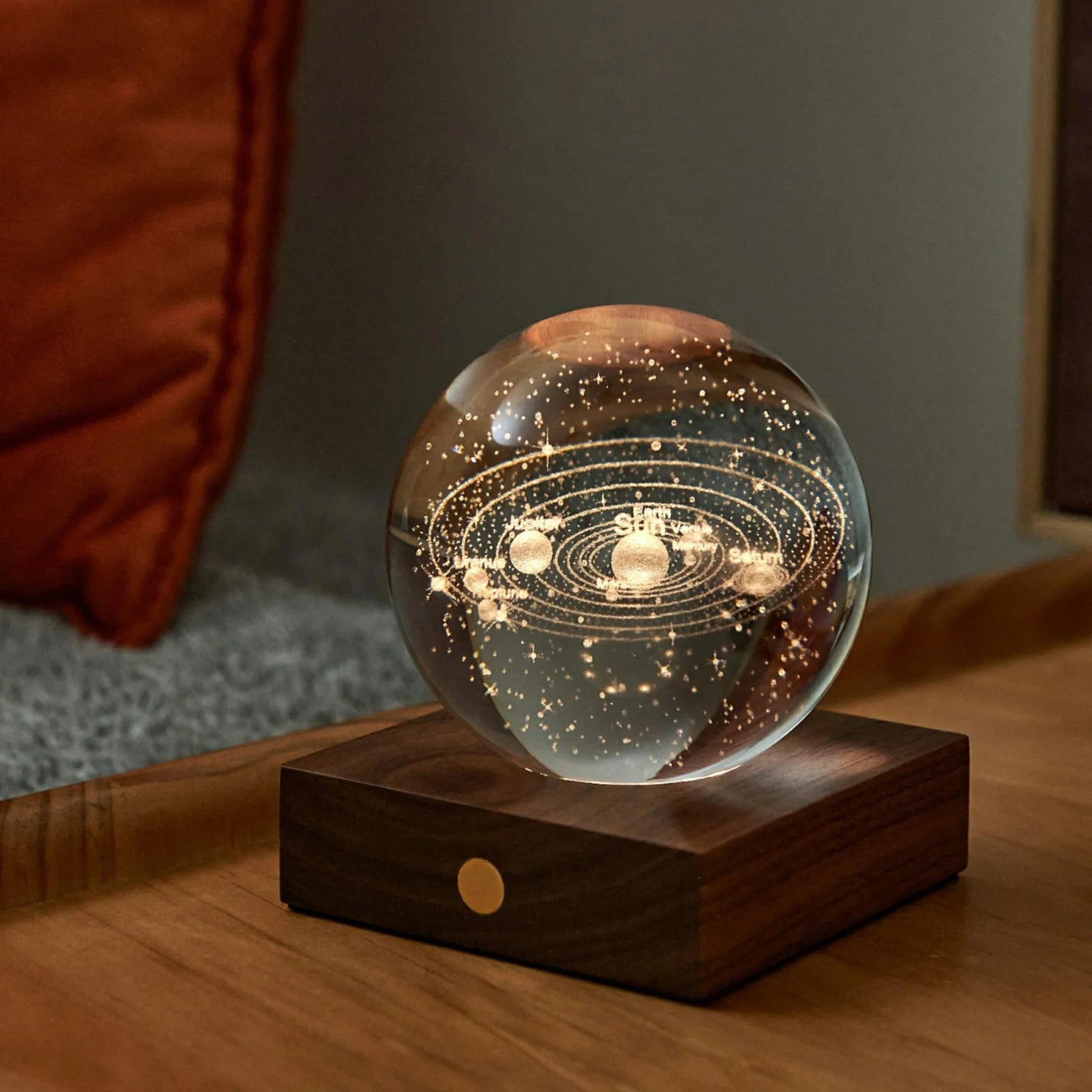 Lampka nocna układ słoneczny w formie przezroczystej kuli na drewnianej podstawie, świecąca w ciemnym pomieszczeniu