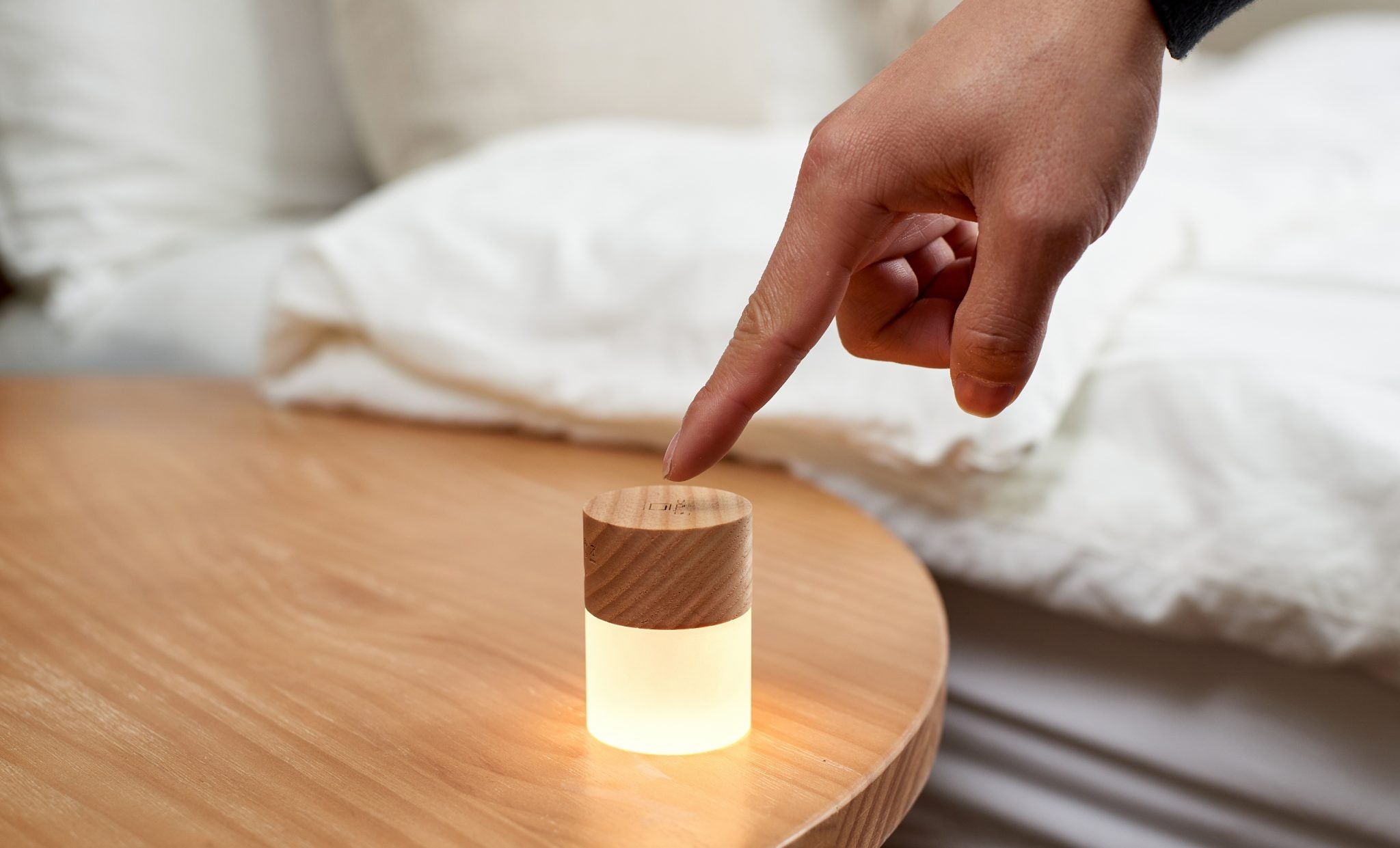 Minimalistyczna lampka nocna z drewna jesionowego dotykana na drewnianym stoliku obok łóżka